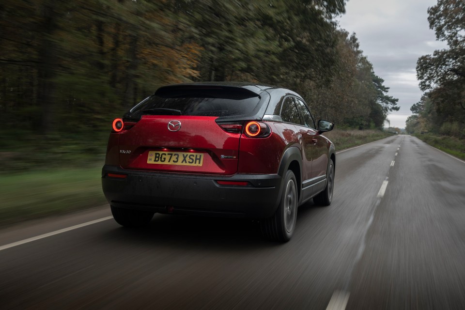 Red Mazda MX-30 driving on a road.
