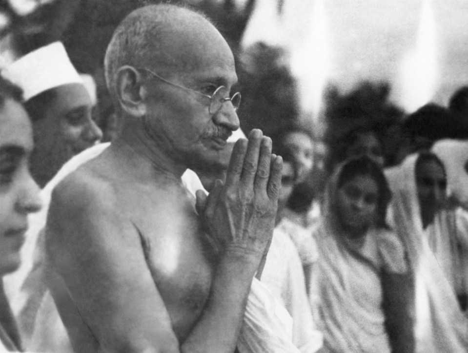 Black and white photo of Mahatma Gandhi greeting people at Juhu Beach.