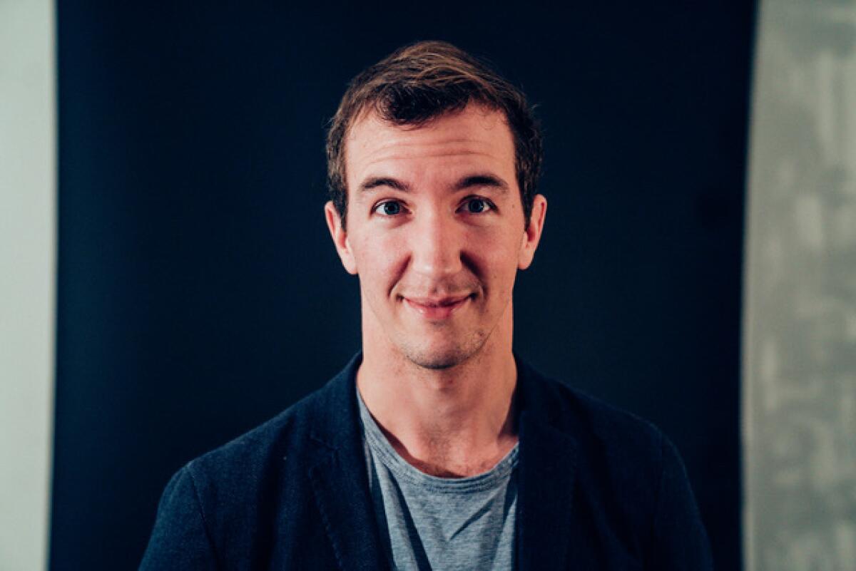 A man smiling in a gray t-shirt and blue blazer.
