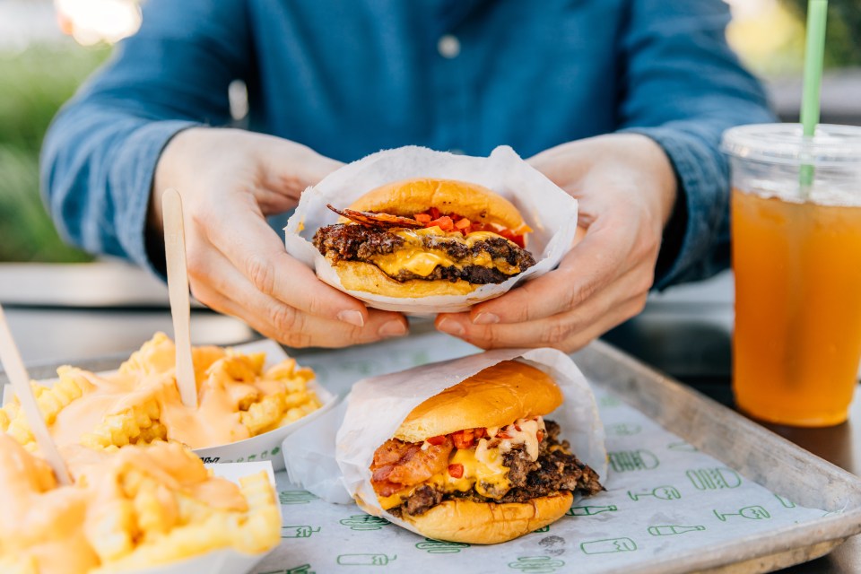 Person holding two cheeseburgers and cheese fries.