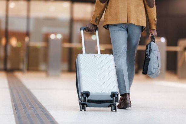 a rear view of a person walking in an airport carrying a wheely suitcase behind them 