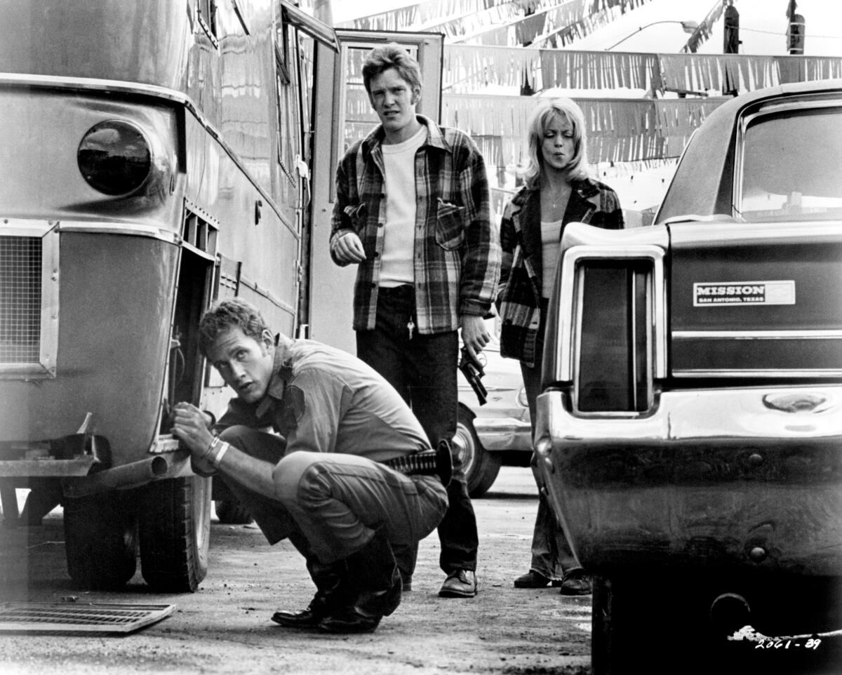Three people walk between cars.