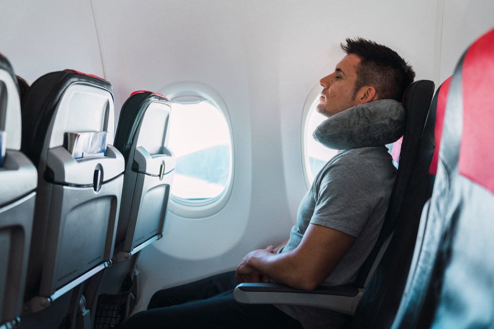 Man sleeping on airplane with neck pillow.