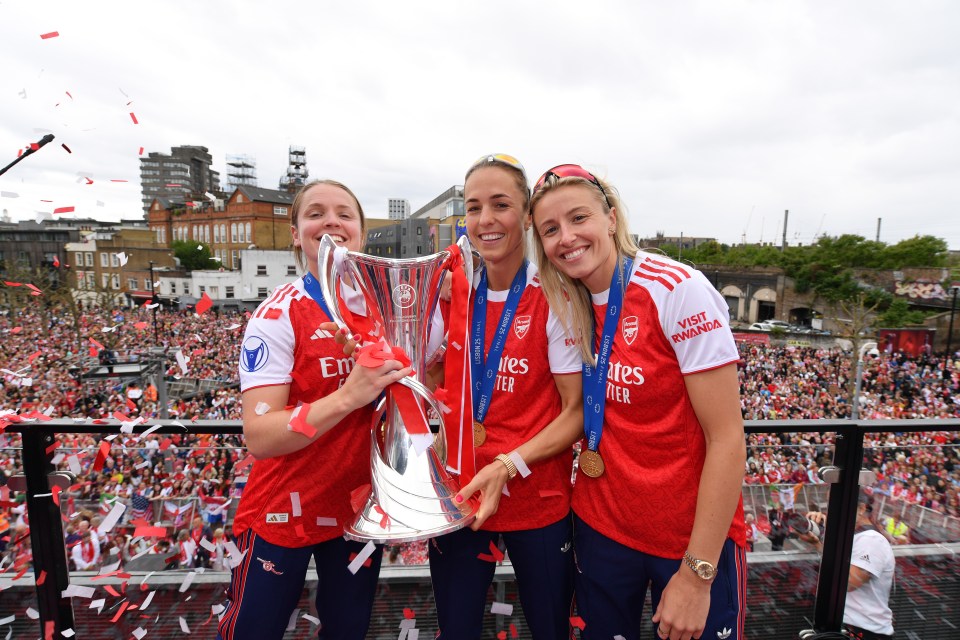 Arsenal's Kim Little, Lia Walti, and Leah Williamson celebrating their UEFA Women's Champions League victory with the trophy.