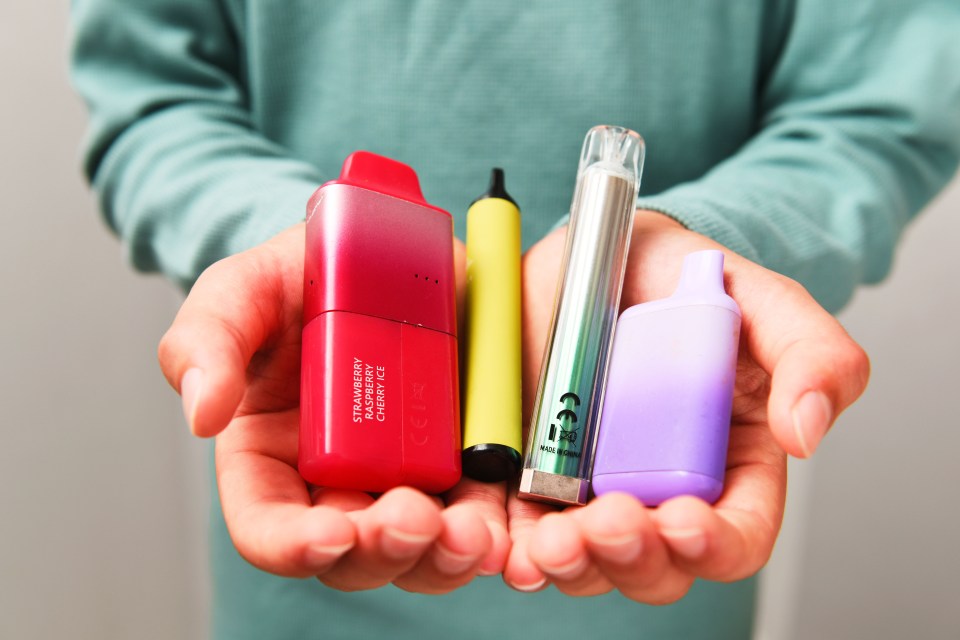 A teenager's hands holding several disposable vapes.