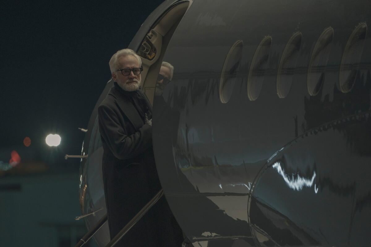 A white-haired man with a beard stares into the distance before boarding a plane