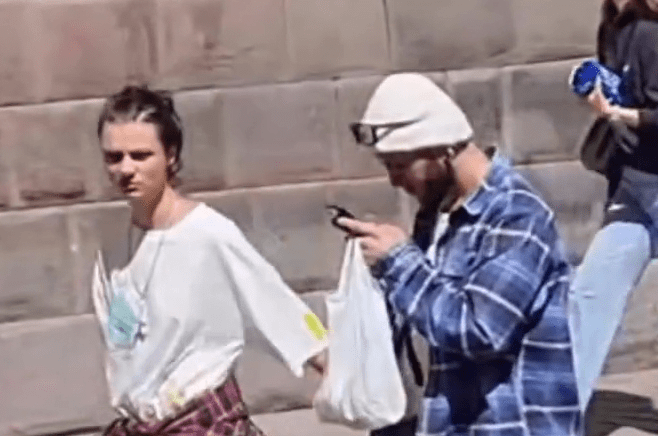 Two people walking down the street, one looking at their phone.