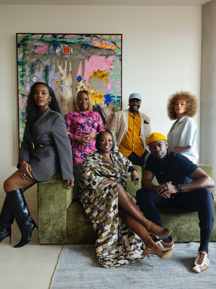 Group photo of six people posing on and around a green couch in front of an abstract painting.