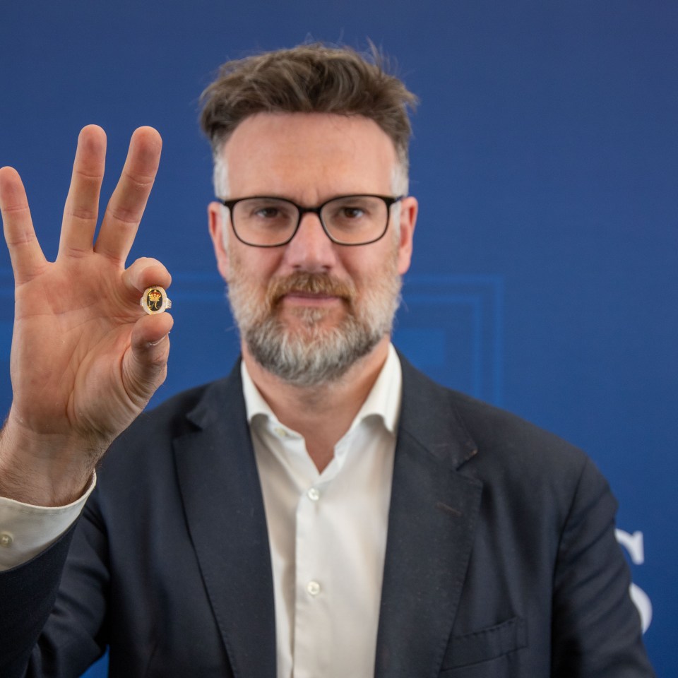 Man in suit holding up a small ring.
