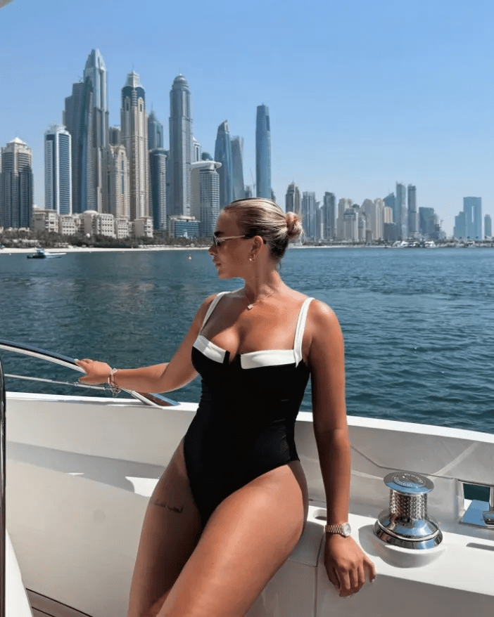 Woman in a black and white swimsuit on a yacht with a city skyline in the background.