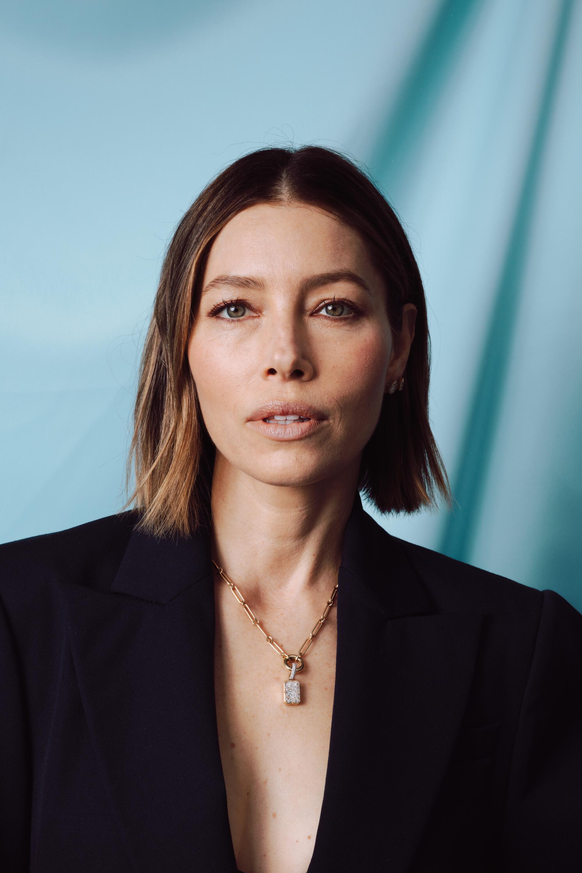 A woman with short hair in a black blazer and golden necklace.