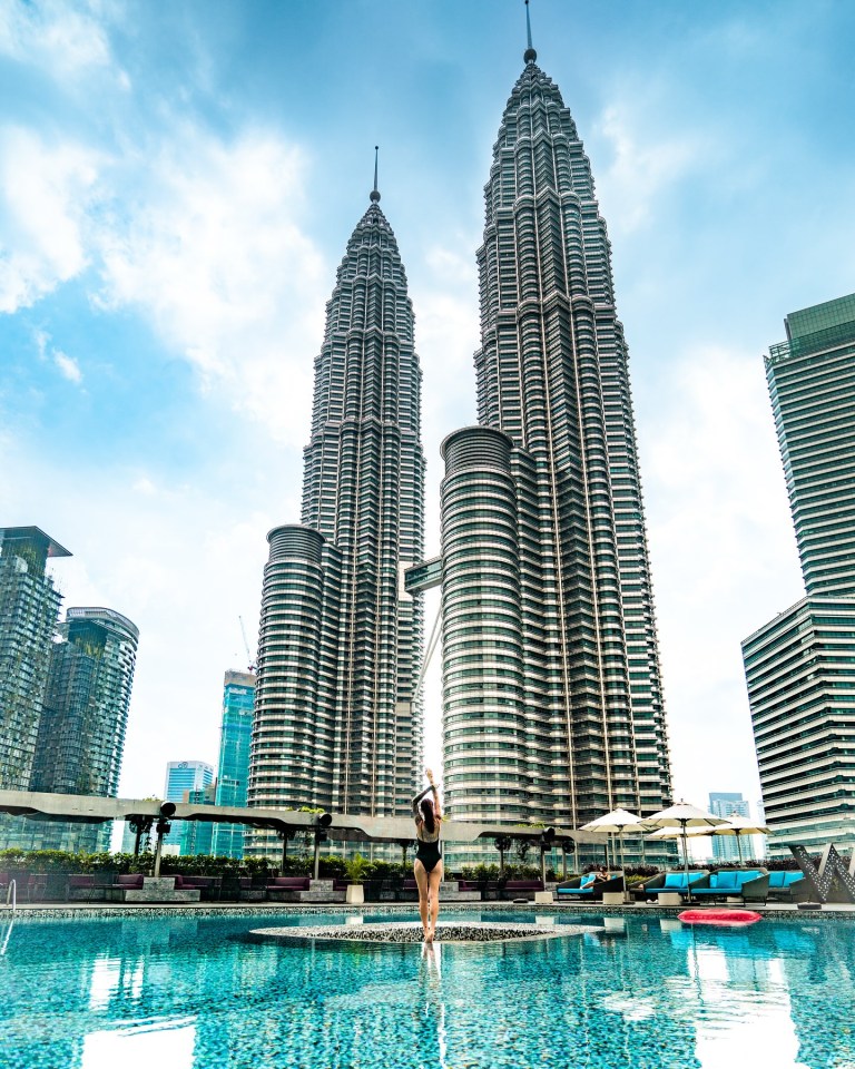 Woman in a swimsuit standing in a hotel pool with the Petronas Towers in the background.