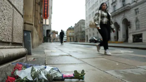Reuters Red roses lie at Water Street by the site of an incident where a car ploughed into a crowd of Liverpool fans during a parade celebrating their side's Premier League win with a woman walking past.