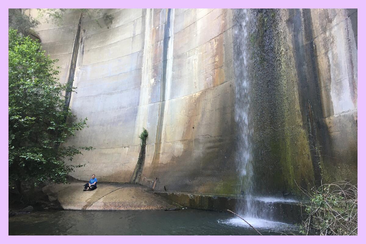 A hiker meditates near a body of water and a dam.