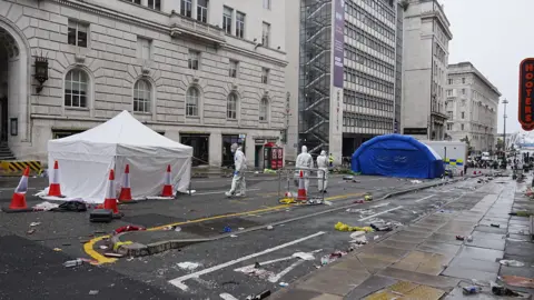 PA Media CSI police officers dealing with an incident near the Royal Liver Building in Liverpool during the Premier League winners' parade. There is much detritus lying on the road.