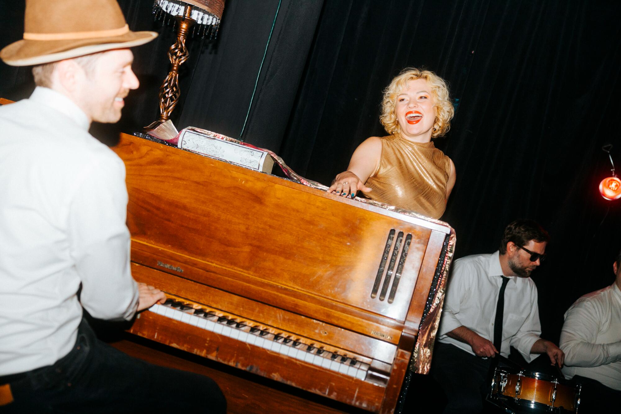 A woman sings propped up on a standup piano.