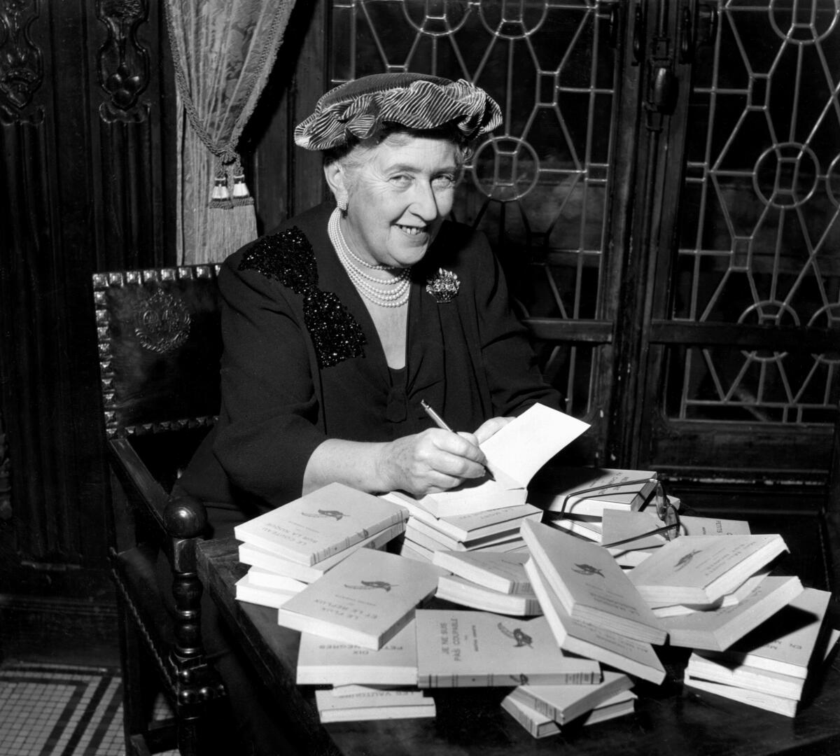 Agatha Christie sits at a desk and autographs books.