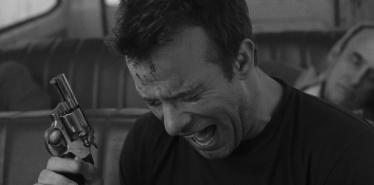 A man with a pistol squints in pain.