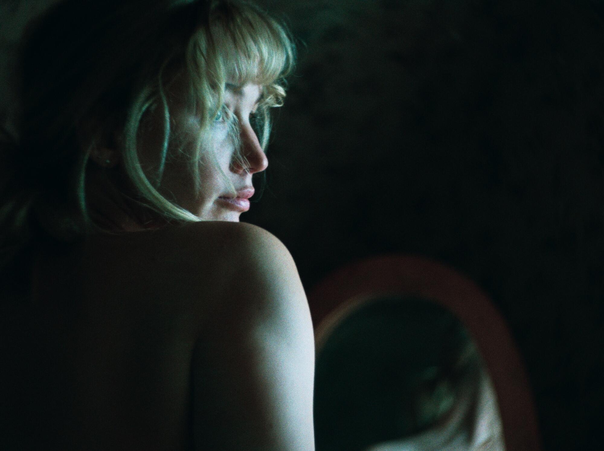 A woman looks over her shoulder, away from a mirror.