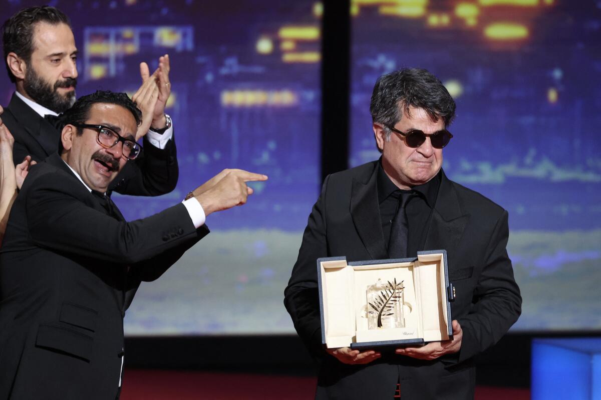 Other men applaud and point to Jafar Panahi, holding the Palme d'Or.