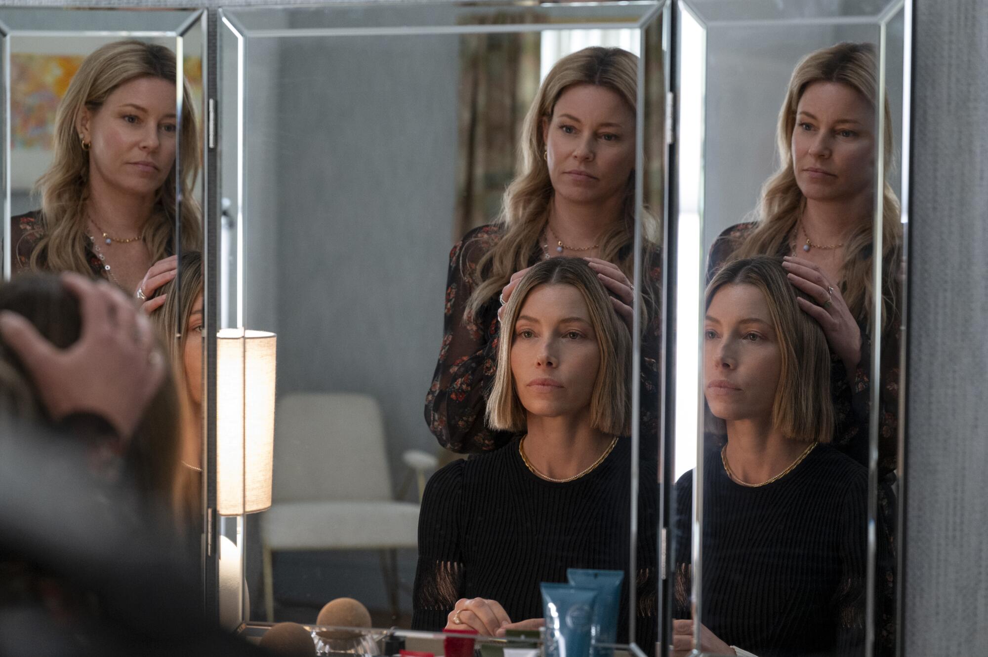 Two women looking at their reflection in the three-sided mirror of a vanity.