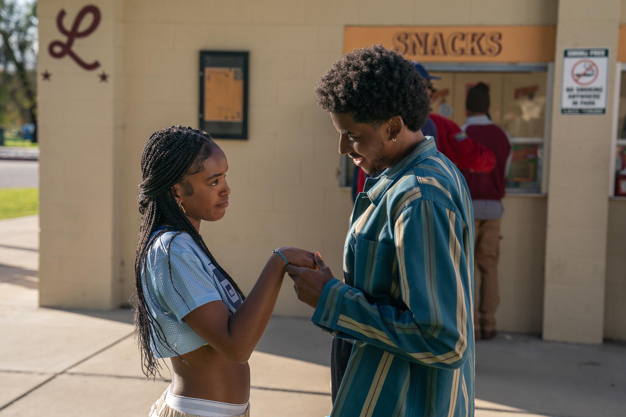 A teenage girl and boy look at each other and hold hands.