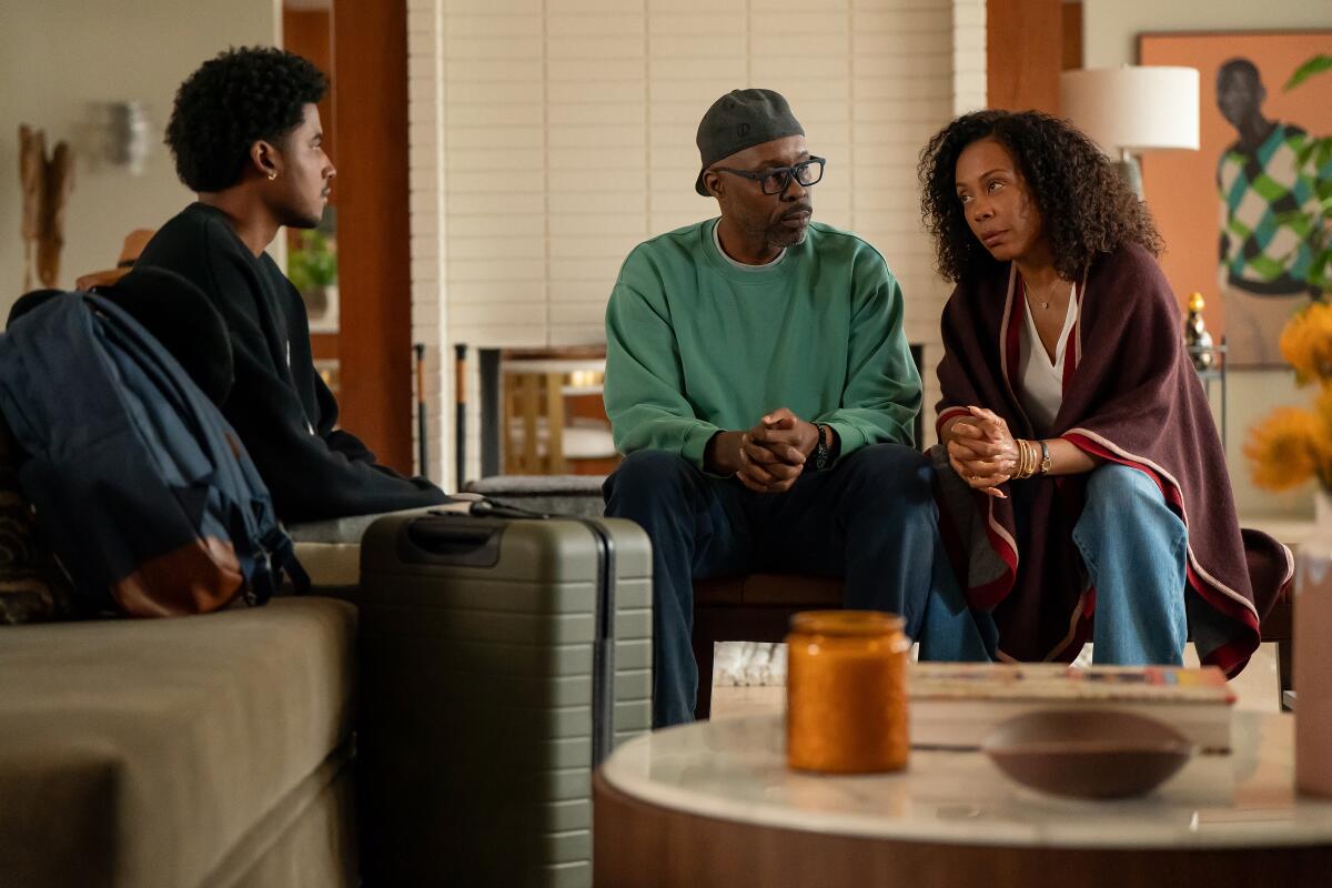 A teen boy sits on a couch with his parents, who are seated across from him.