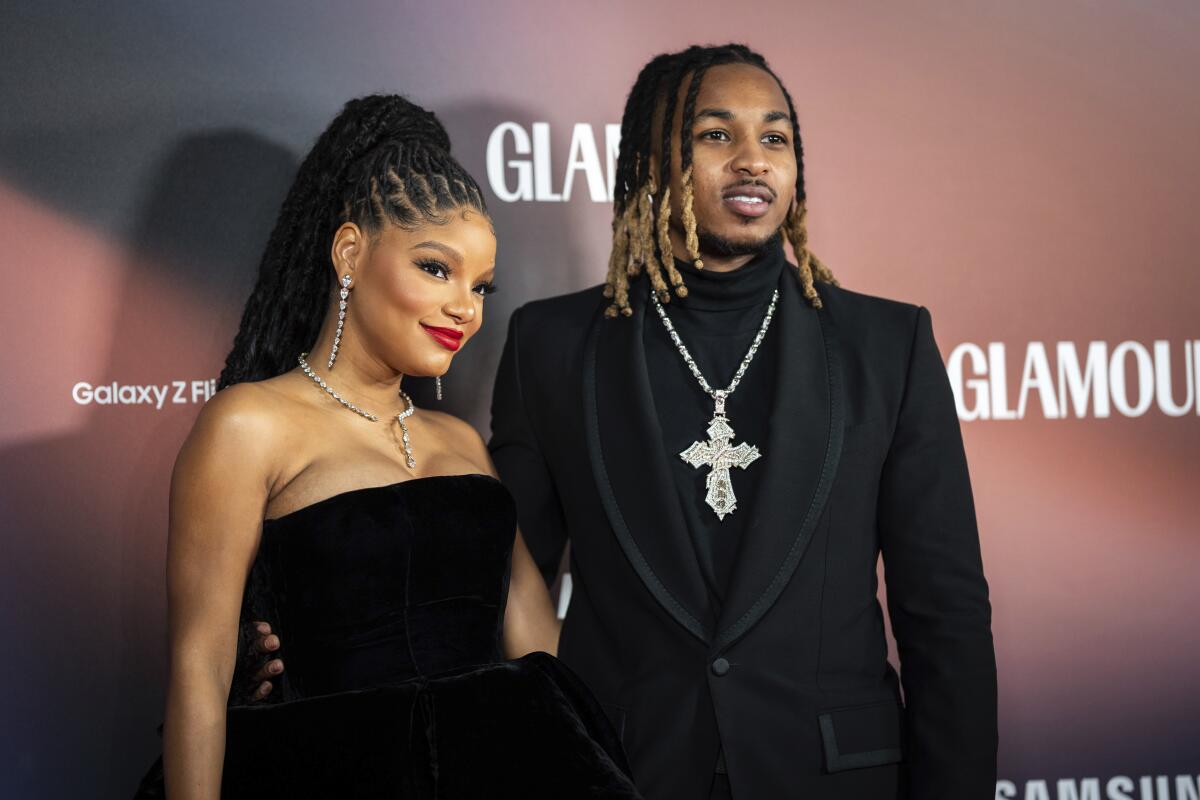 Halle Bailey in a black strapless dress next to DDG wearing a dark suit