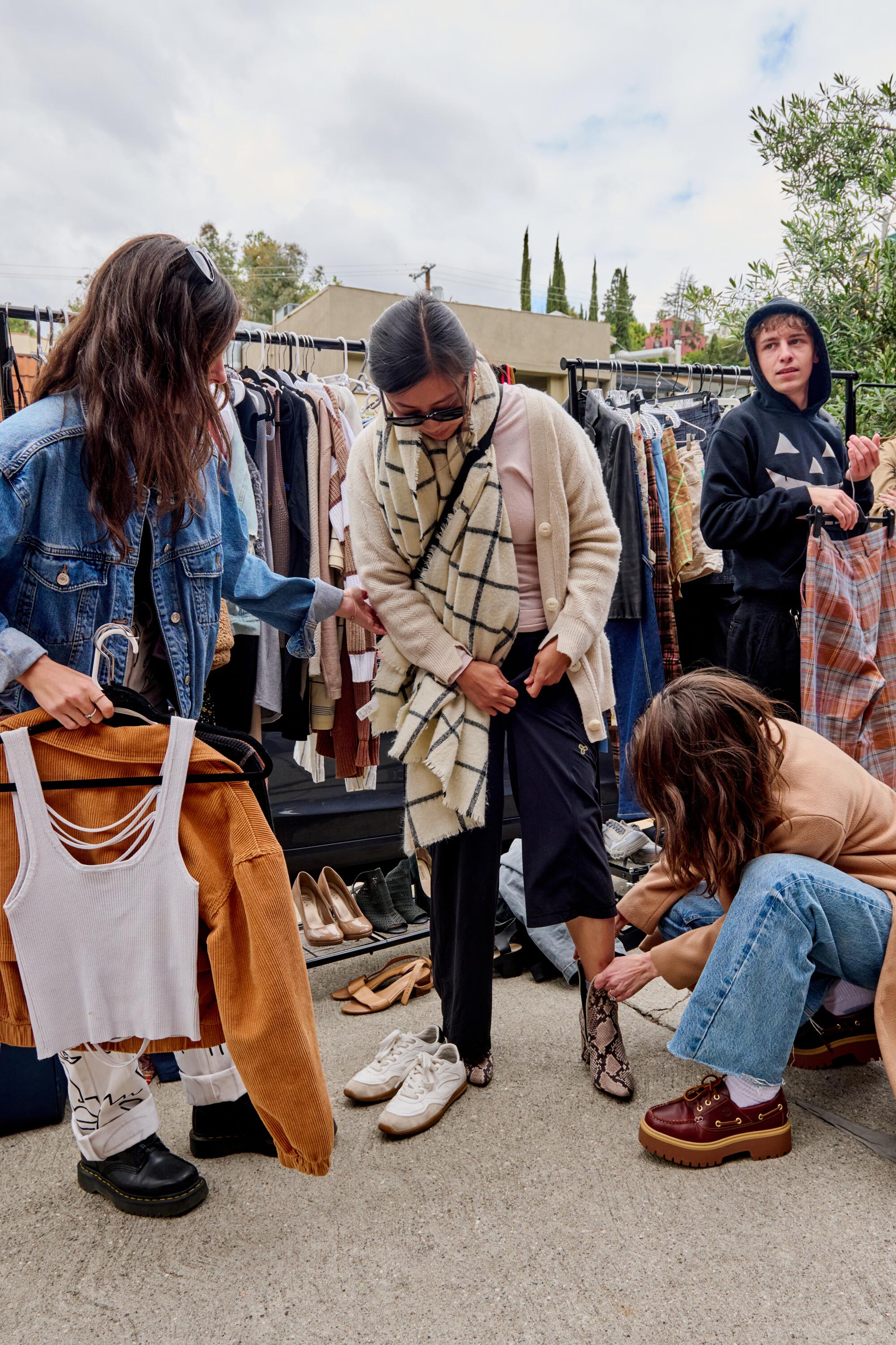 Two women help another woman try on some shoes.