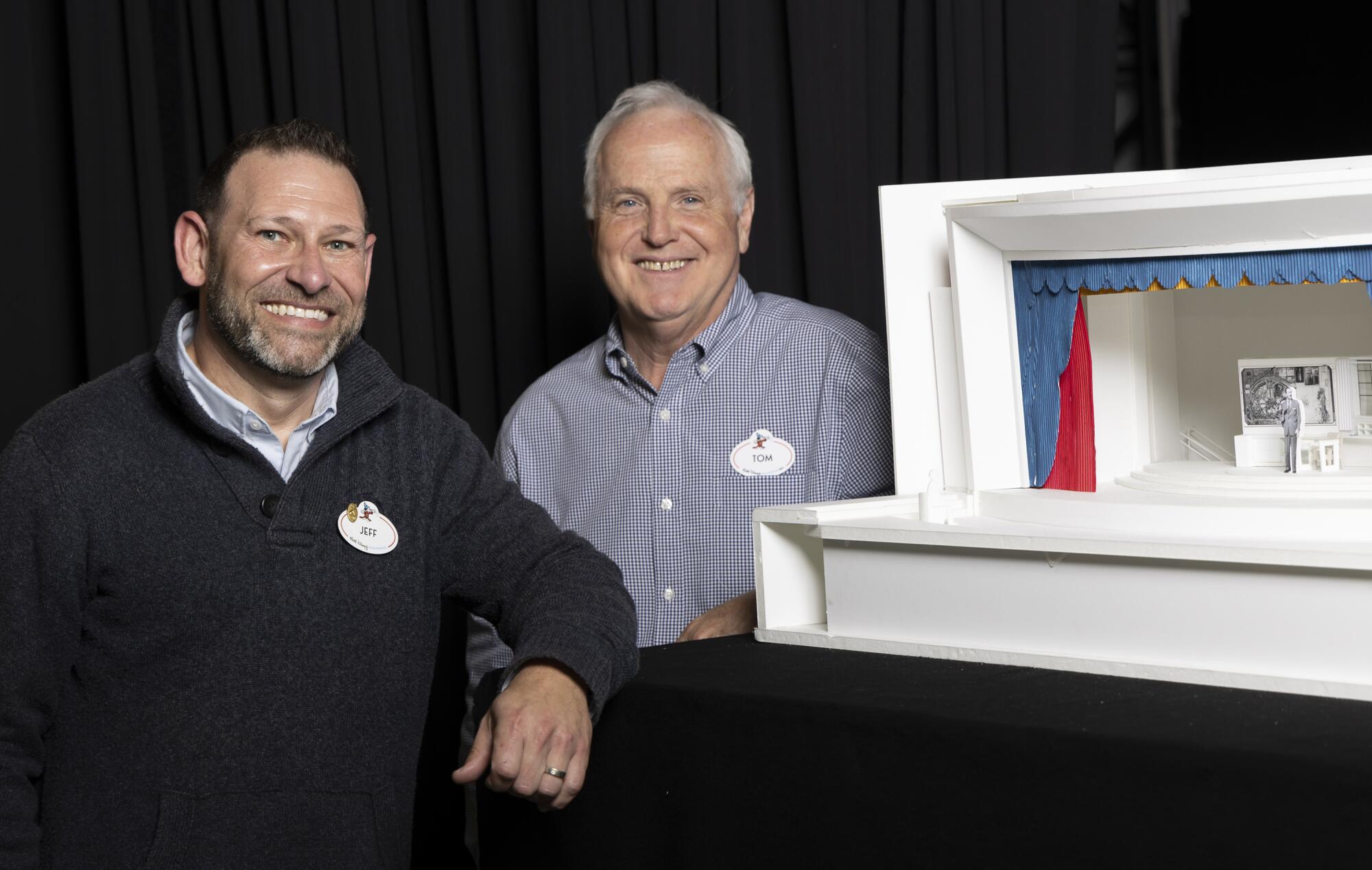 Two male Disney designers standing next to a model of a theater.