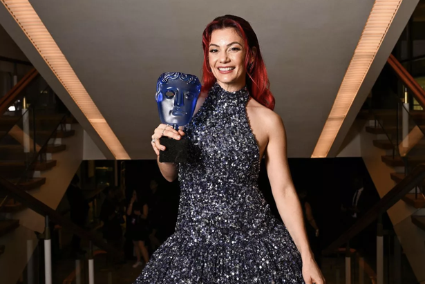 Dianne Buswell posing with her BAFTA award while wearing a blue sparkly dress