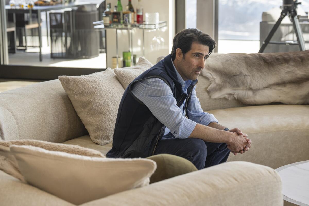 A man in a blue vest and shirt sitting on a big beige couch.