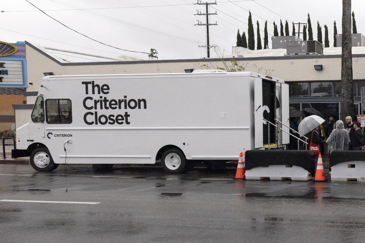 A white truck is parked in front of a video store and theater.