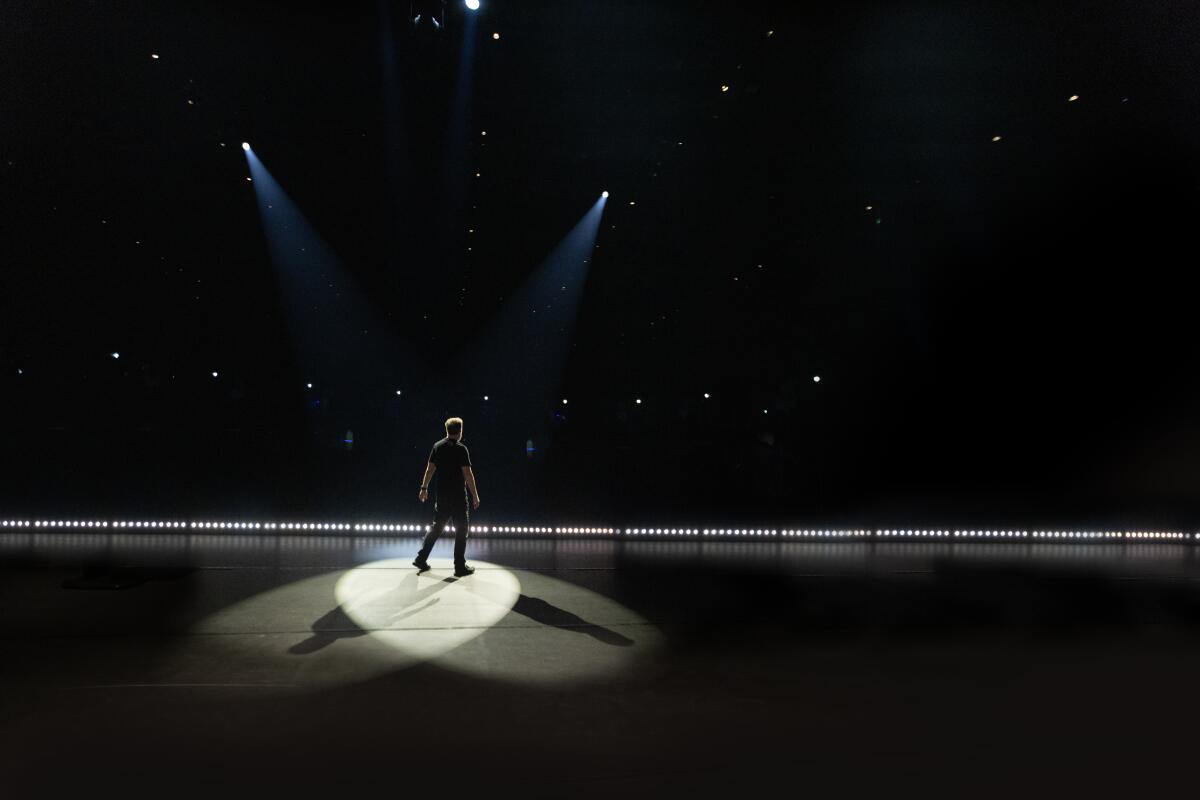 Ricky Gervais stands onstage with two spotlights shining down on him