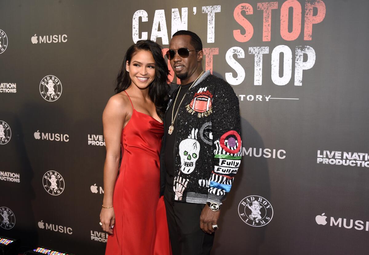 Cassie in a red sleeveless gown posing next to Sean "Diddy" Combs in a black jacket and sunglasses at a red carpet event