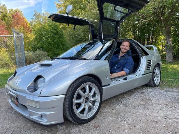 James Engelsman in a blue shirt sat in a silver car with the door open.