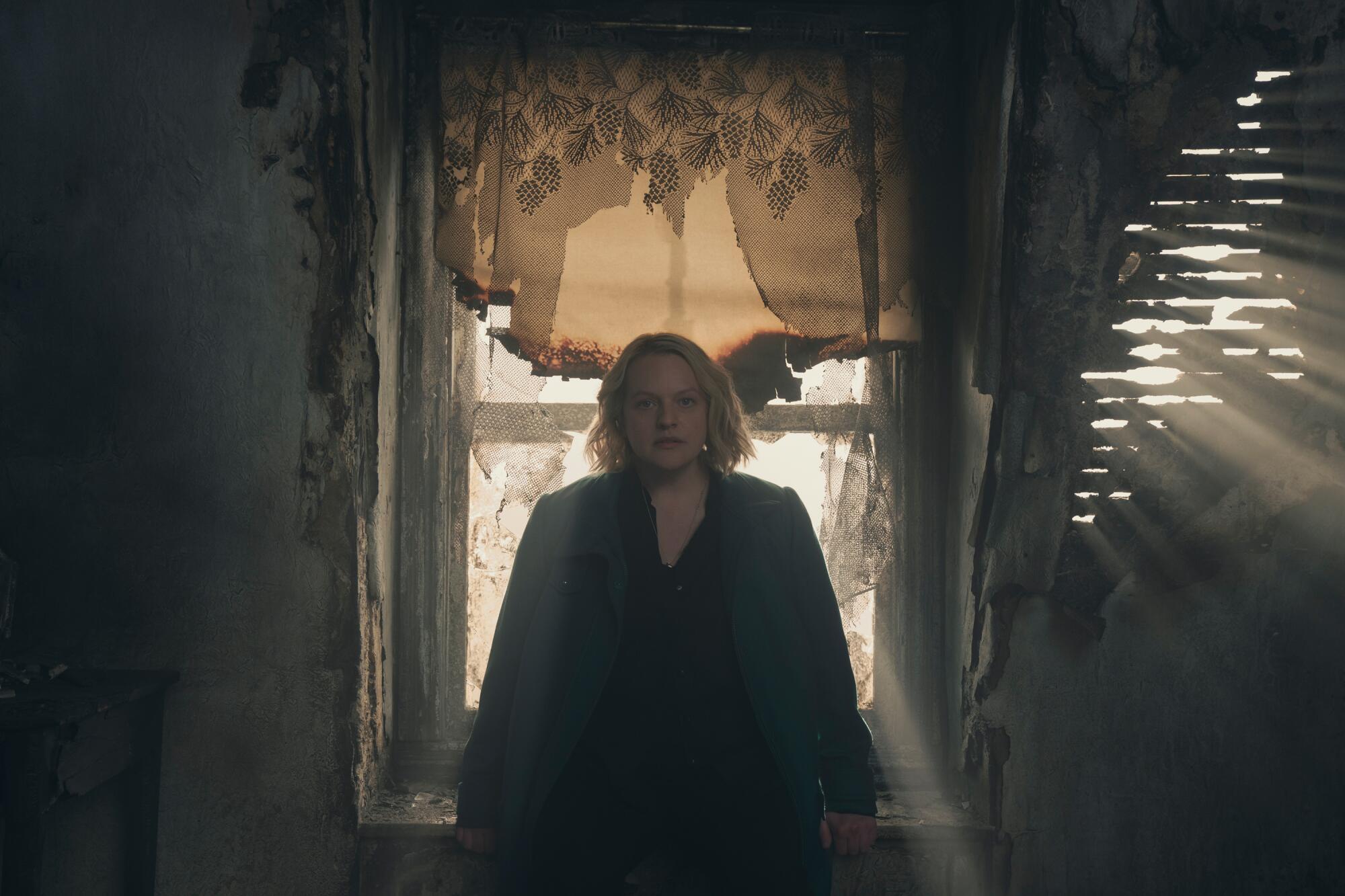A woman sits against a window sill in a dim room