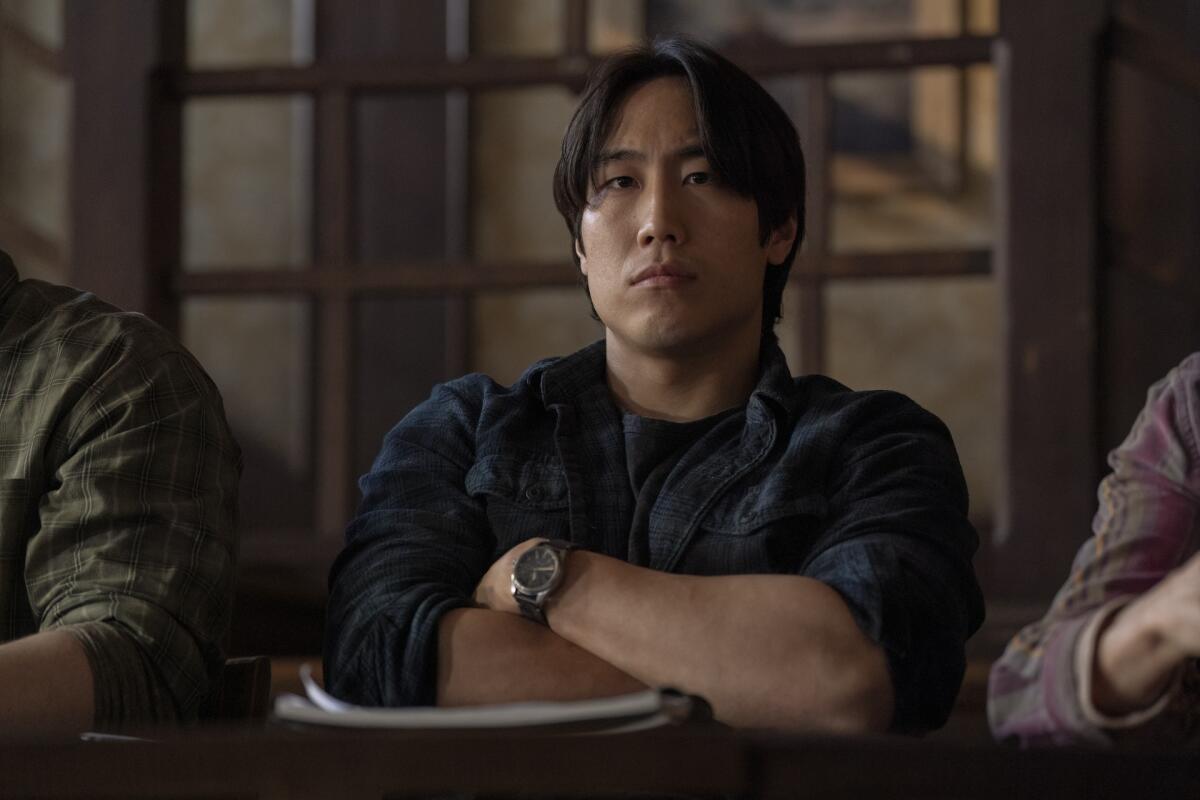 Young Mazino looks angrily ahead with his arms crossed in front of him