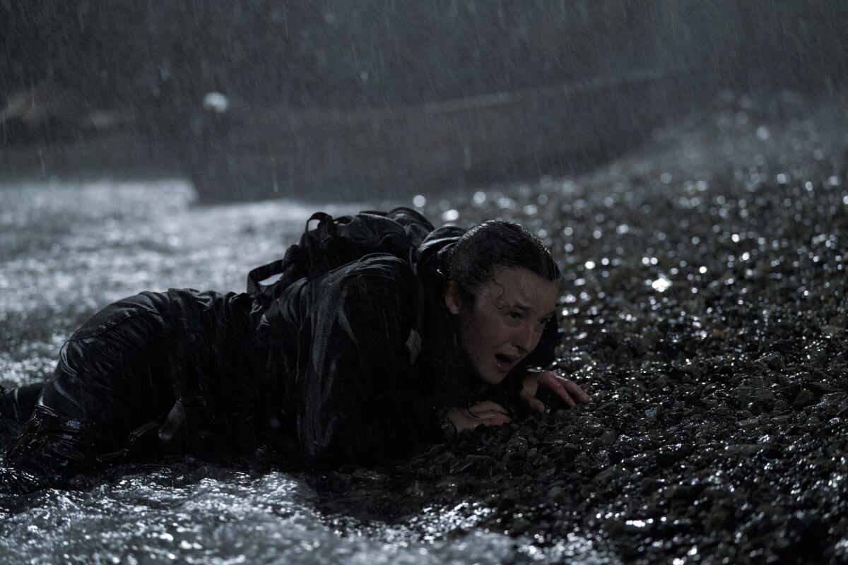 Bella Ramsey crawling on a beach in a storm