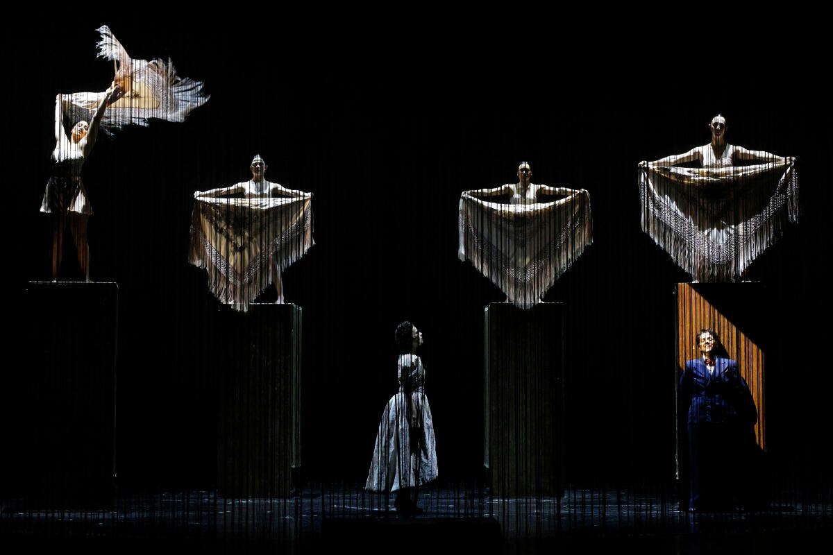 Two characters sing onstage as ghostly figures seem to hover above.