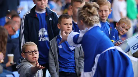 Getty Images An Everton toffee lady, wearing a traditional blue dress and white pinny, gives out sweets to young Everton fans at Goodison Park.