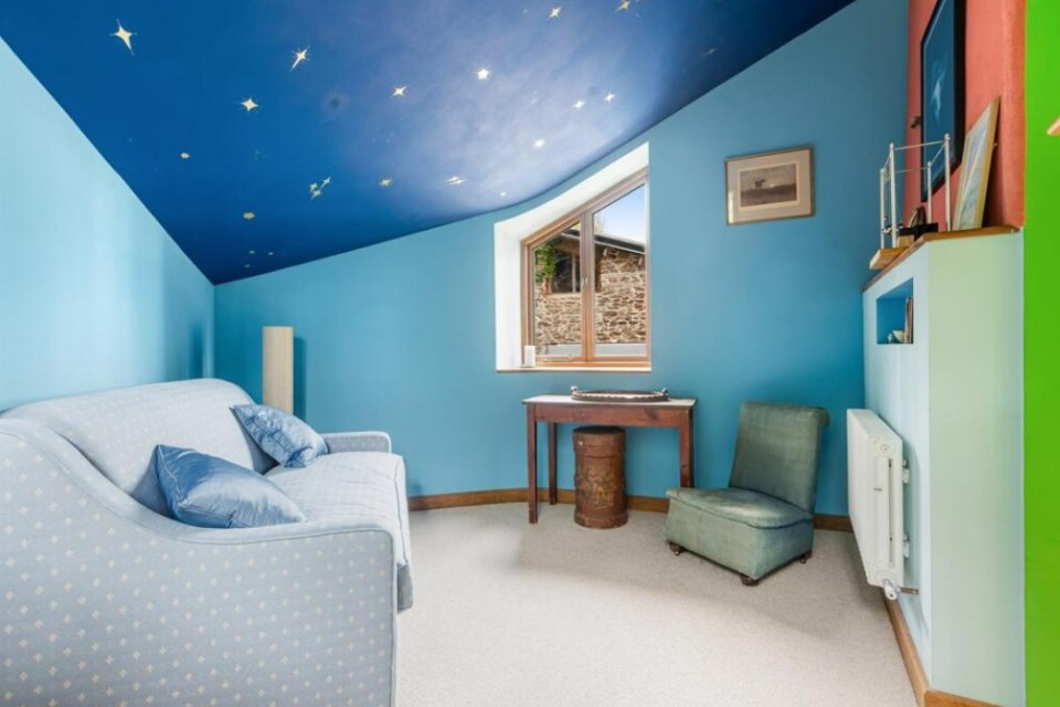 Interior view of a room with light blue walls, a star-painted ceiling, a light blue couch, and a small wooden desk.