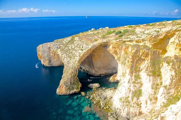 Small boats with passengers and natural rock formations of Blue Grotto, on southeast coast of Malta.  Every day from sunrise until about 1 pm a unique sight can be observed here: location of cave combined with sunlight lead to water mirroring showing numerous shades of blue. Several caverns mirror brilliant phosphorescent colours of underwater flora; other caverns show a deep dark shade of blue.  Popular destination for tourists with boat trips to visit caves, scuba diving snorkeling and rock climbing being most popular activities here.