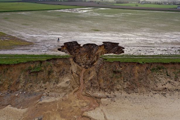 HAPPISBURGH, ENGLAND - JANUARY 27: A man walks his bicycle past a recent landslip on the cliff edge and beach in the village of Happisburgh on January 27, 2021 in Happisburgh, England.  Erosion of the Norfolk sandy cliffs and sand dunes has caused many buildings and farmland to be lost to the sea. The effects of global climate change causing storms and sea swells has seen the East Coast of the United Kingdom lose up to one metre of coast line each year.  (Photo by Christopher Furlong/Getty Images)