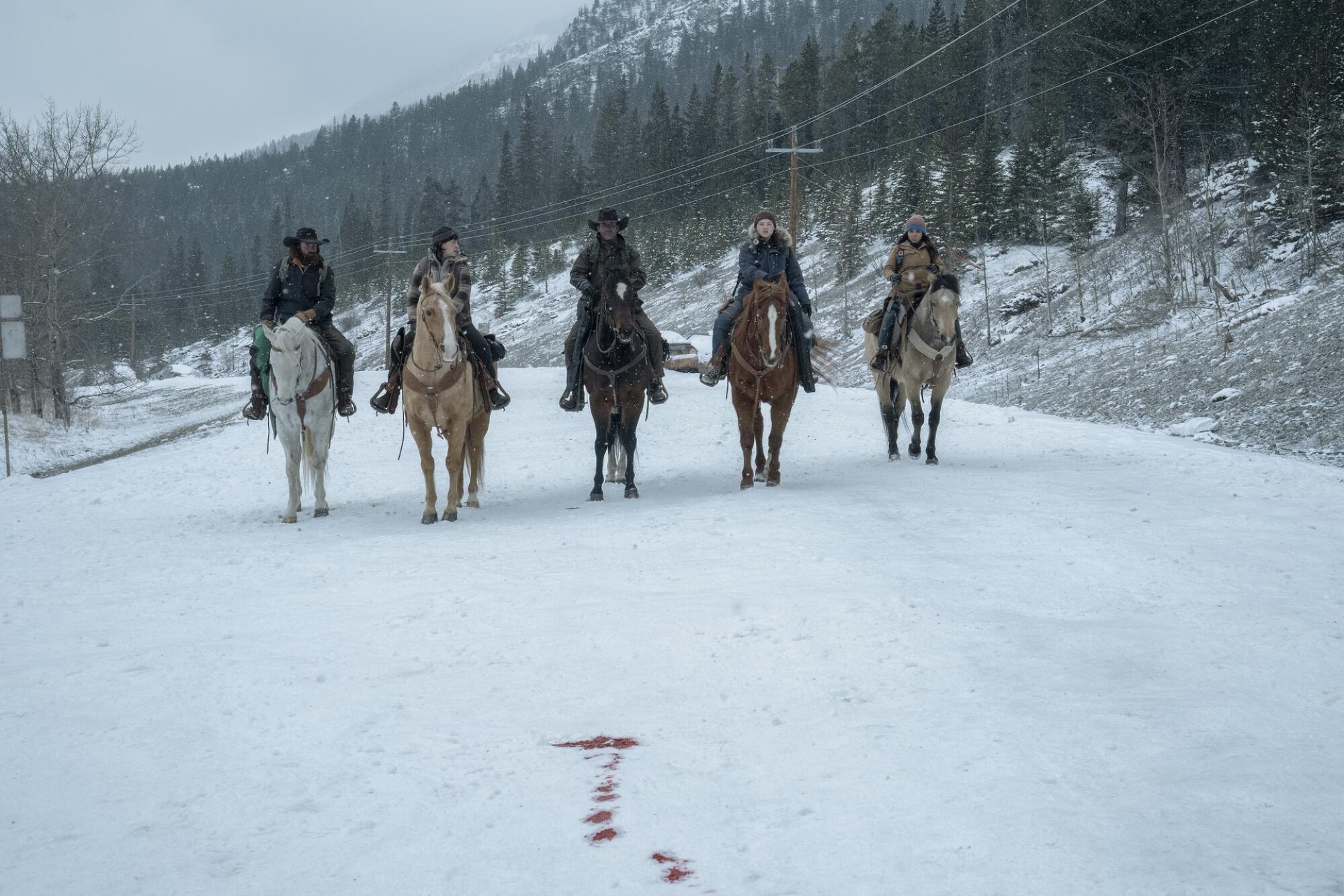 Five people ride horses on a snowy road, heading toward the camera