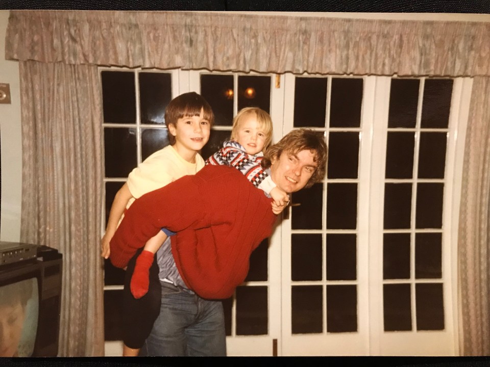Photo of a man carrying two young children on his back.
