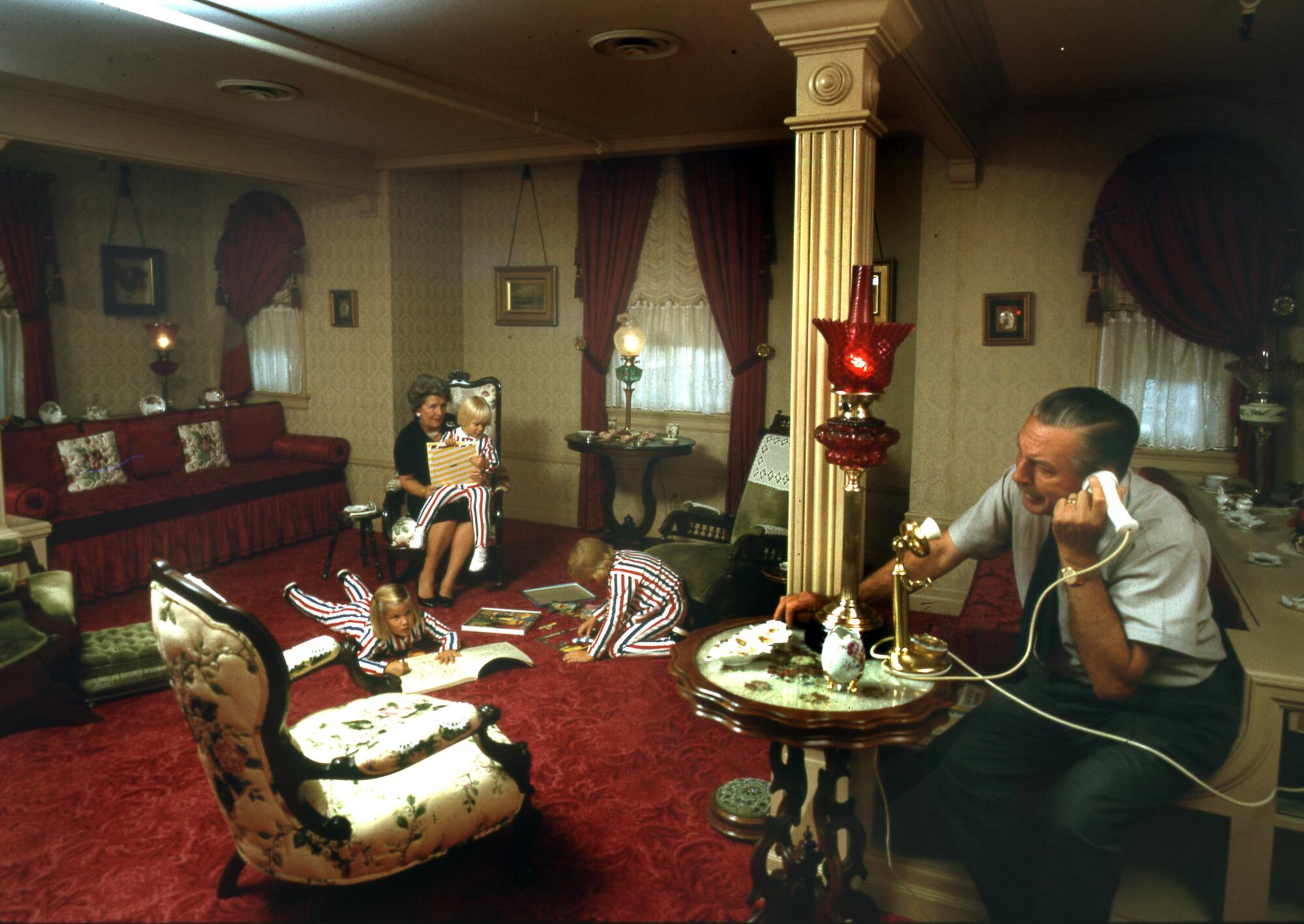Walt Disney talks on the telephone while his wife, Lillian, plays with three of their grandchildren