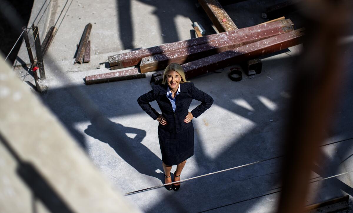 A woman with her hands on her hips stands in a construction site looking up. 