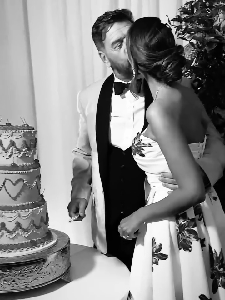 Black and white photo of a couple kissing at their wedding, cutting a cake.