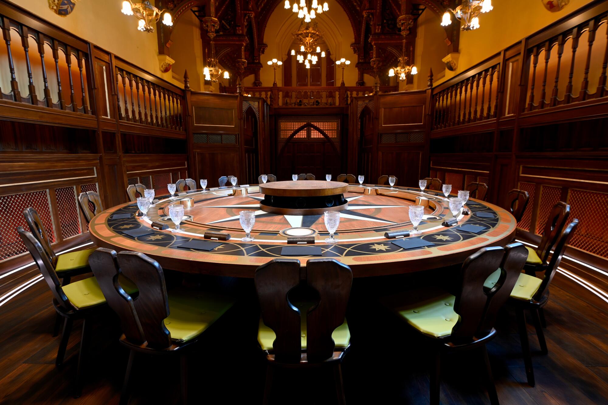 A large round wood table set with crystal goblets and surrounded by wood chairs in a Gothic-style room